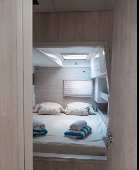 A neat double guest cabin with twin pillows, folded towels and a skylight hatch above the bed