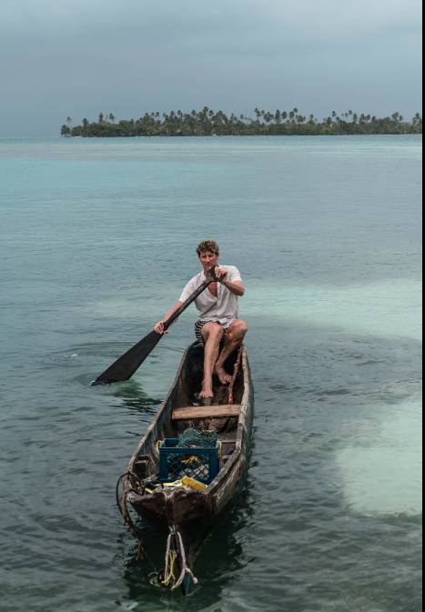 A crew member in a Panama hat holding two fresh fish over calm Caribbean water