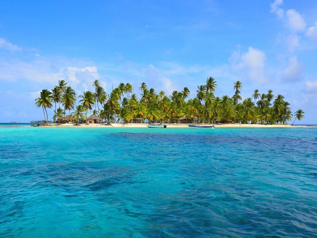 Clear Caribbean shallows lapping a palm island under a bright blue sky